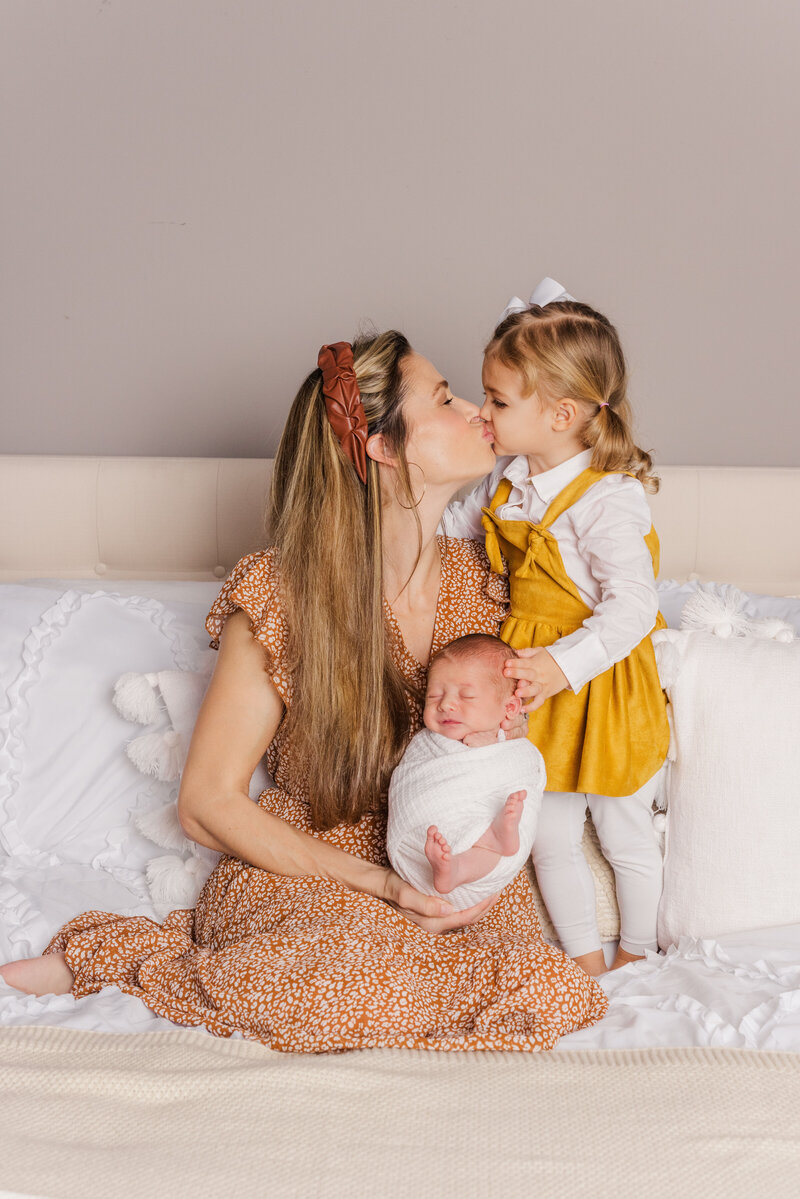 Mom kisses daughter while holding newborn for portrait session in Richmond.