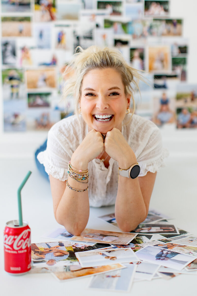Photographer Brooke Tucker, specializing in play based family photography, smiling in a bright and creative space, surrounded by printed photos and a classic Coca-Cola, ready to connect with clients and bring their family memories to life.  