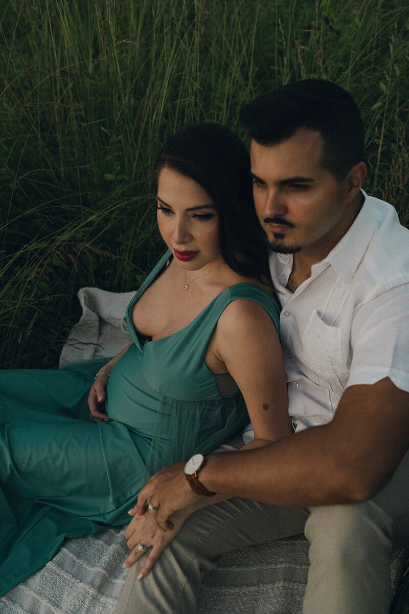 soon to be mother and father sitting in a field looking in the distance