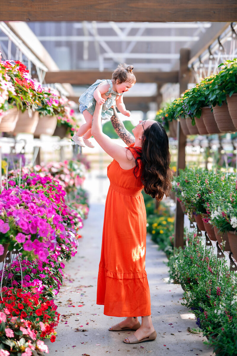 Mother lifting her baby girl among vibrant flowers during a golden hour family session in McKinney, Texas, photographed by Jennifer L. Kirk Photography.