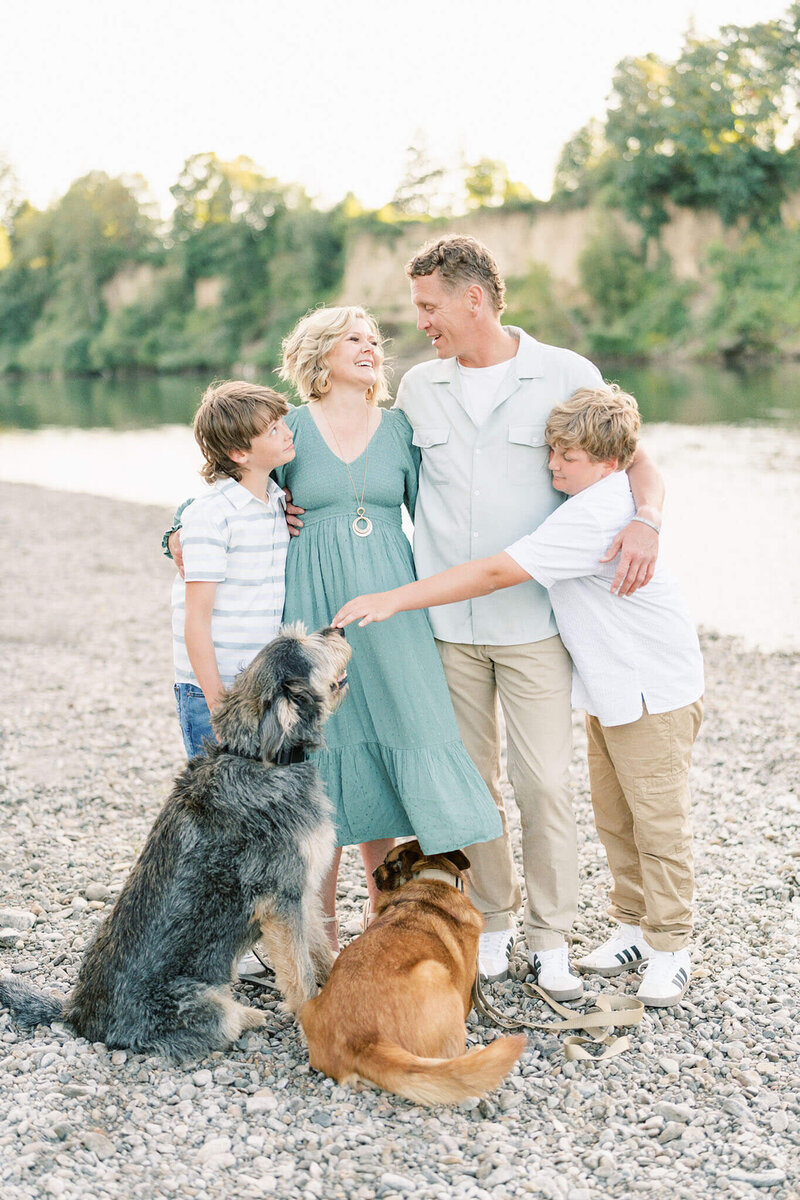 candid family photo of a family playing on the riverside with their two dogs
