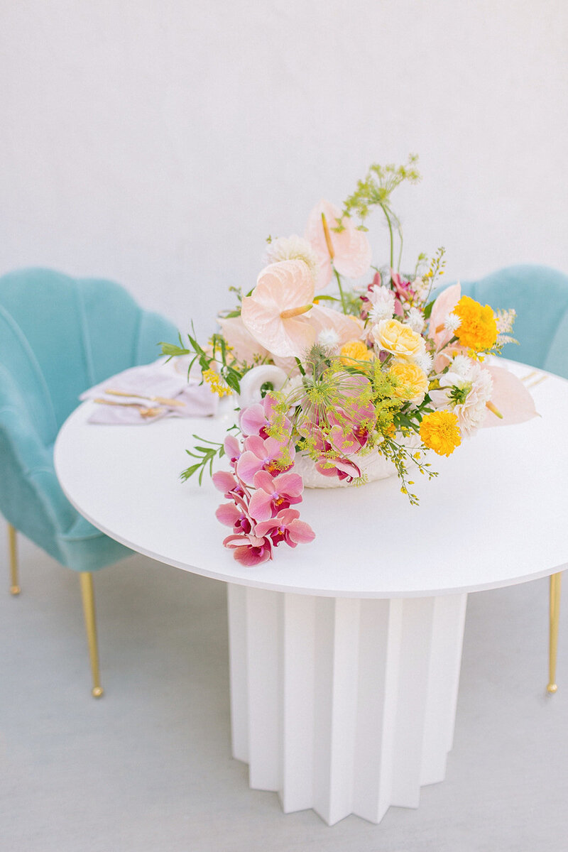 Bright and colorful floral arrangement sitting on a white table beside two blue chairs