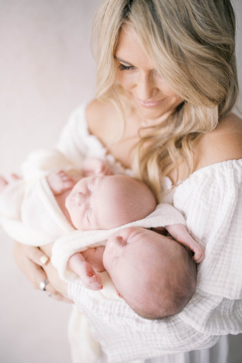 Newborn portrait taken in a studio in Jacksonville of mom wearing a blue floral dress laying down and cuddling her sleeping newborn baby boy swaddled in all white