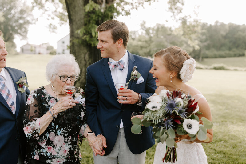 A bride and groom wedding photograph laughing at their grandmother sipping champagne at Missouri Kuhs Farm wedding