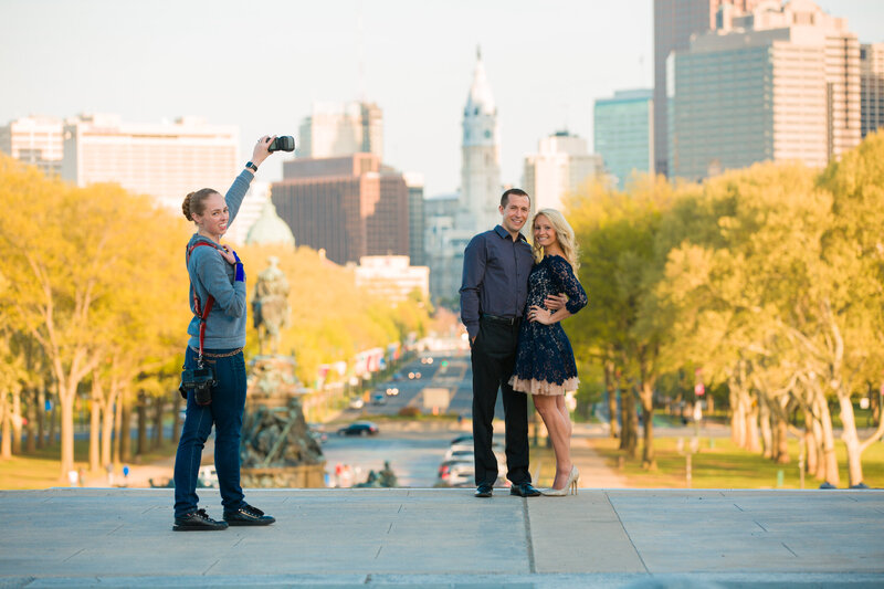 Jen Stitt holding an off-camera flash at the Philadelphia Museum of Art during an engagement session, showcasing her expertise in lighting techniques to create stunning and professional couple portraits at this iconic location.