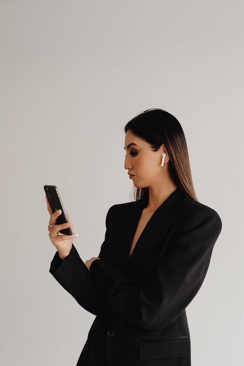 kaboompics_dark-classy-aesthetic-fashion-beautiful-asian-female-entrepreneur-in-black-suit-technology-and-devices-iphone-laptop-airpods-30086-min