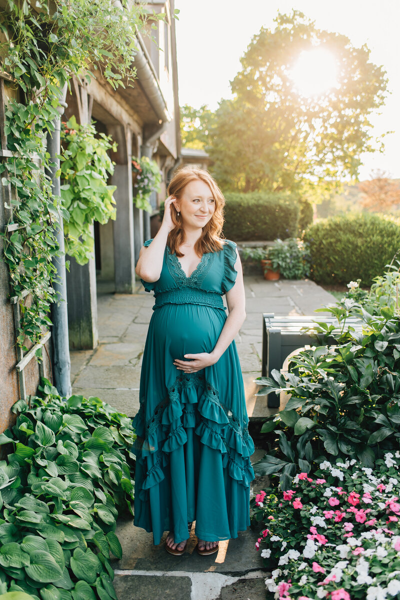 Expecting mom in teal dress smiling off camera at sunset
