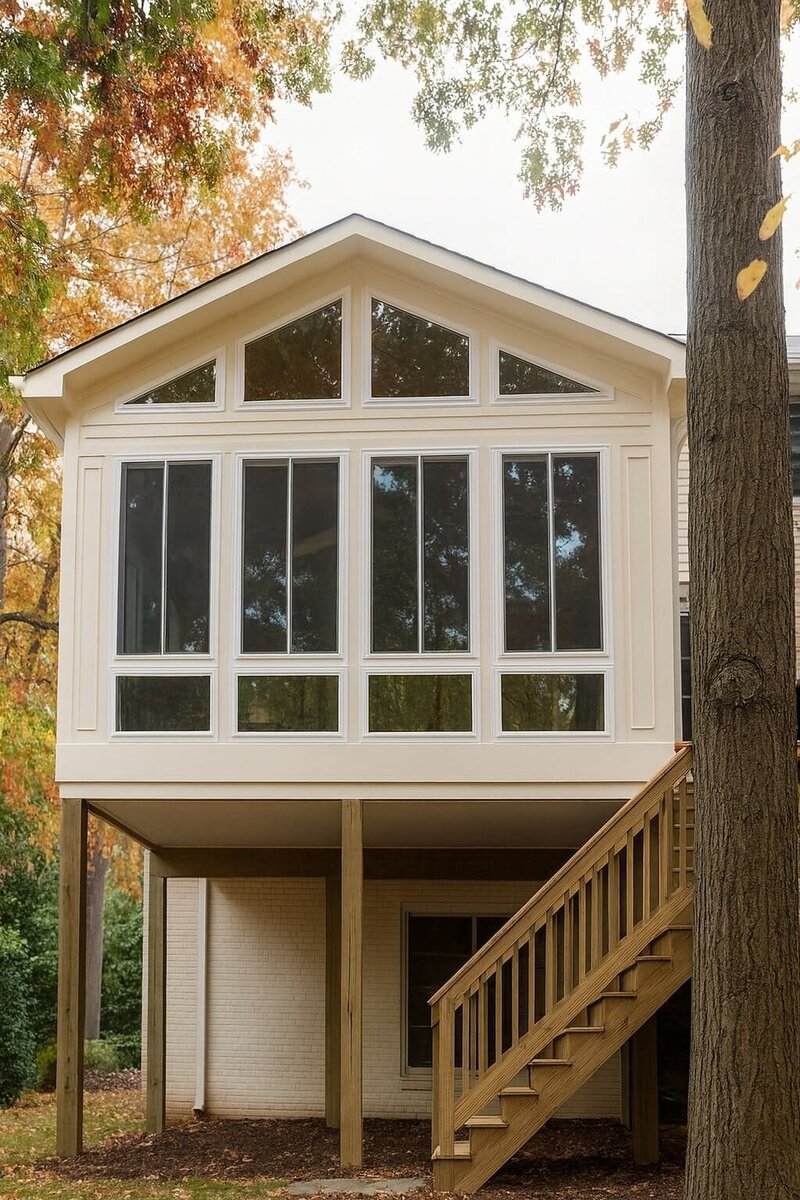 Sunroom extension with expansive windows and raised foundation overlooking a wooded backyard.