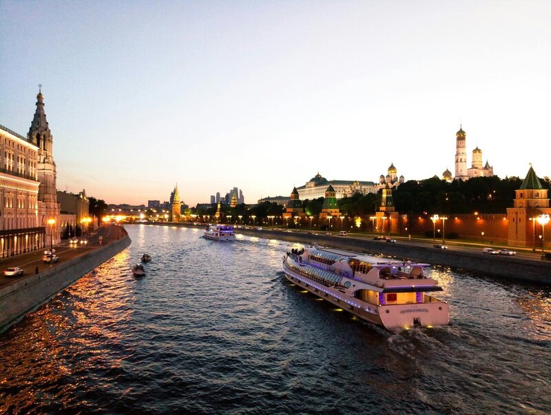 River cruise boat sailing through a European city at sunset with glowing skyline