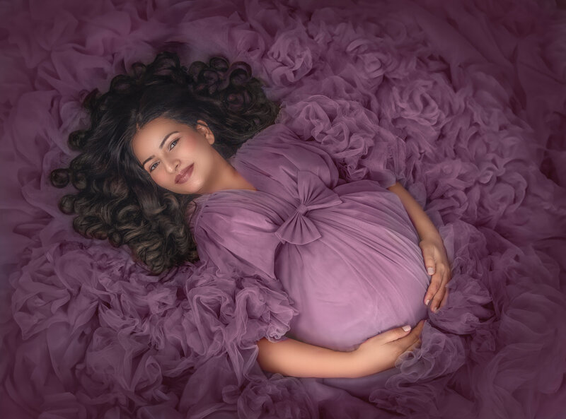 "Pregnant mom beautifully posed lying down in a luxurious gown, looking directly at the camera, captured in a timeless maternity photography session in Ottawa."