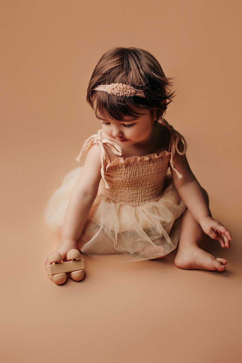 Baby holding plush toy while smiling on textured blanket backdro