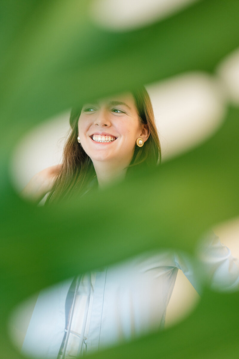 portrait of matilyn smiling beside a large leaf of a monstera deleciosa