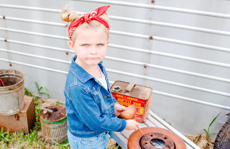 Young girl in a garage theme session with antique gas cans giving her best tough face