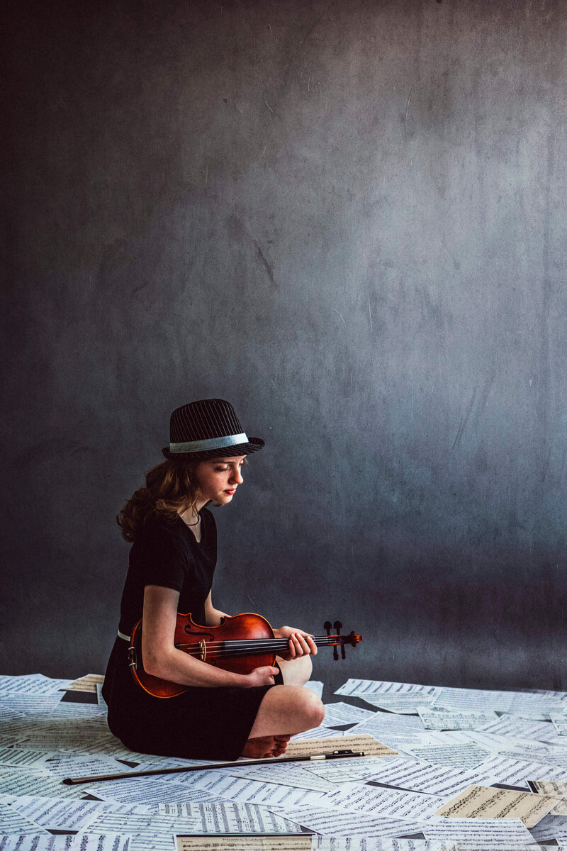 girl sits on sheets of music holding violin