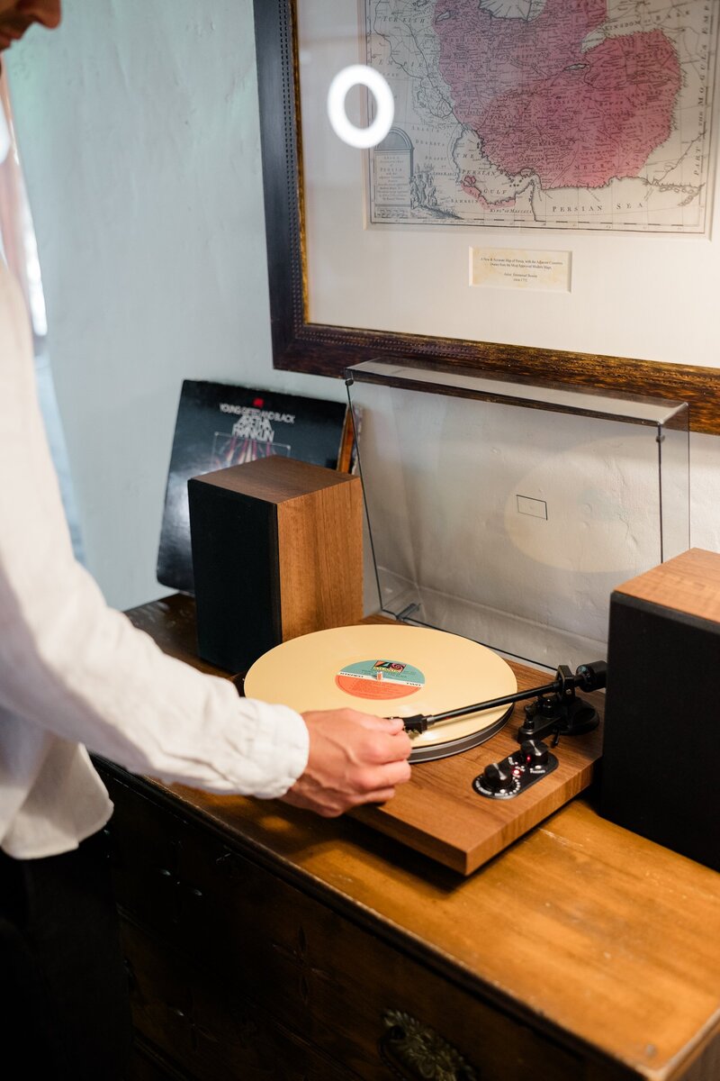 A groom places a vinyl on a wooden record player 