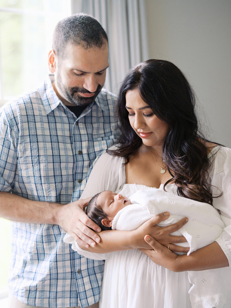 A mother holding her newborn as the mother and father look down at the newborn by Katie Stansfield Photography, a Richmond newborn photographer.