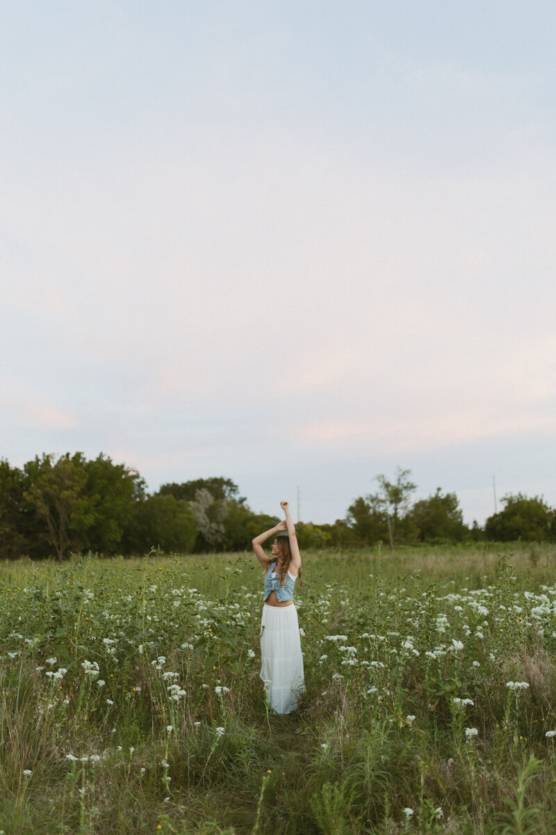 A high school senior dancing joyfully in a vibrant field of wildflowers in Wichita, KS, capturing the freedom and beauty of this special milestone moment.