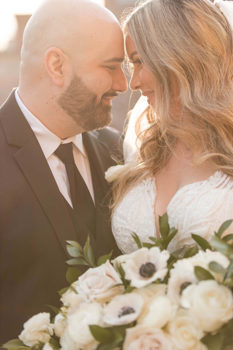 Bride and groom facing each other with their foreheads close by.  Cuban-Americans in their wedding clothes as the bride holds her bridal bouquet.