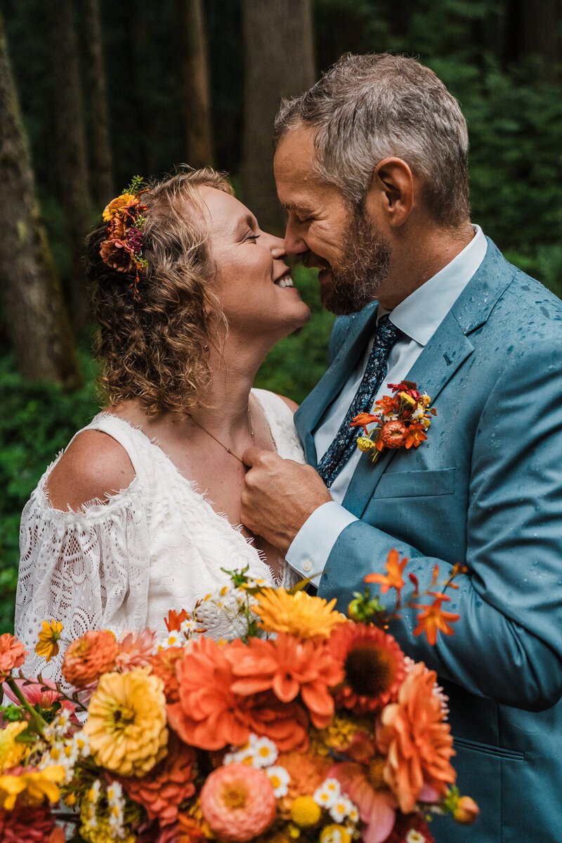 a bride and groom embrace after their forest ceremony in olympic national park with bright warm florals