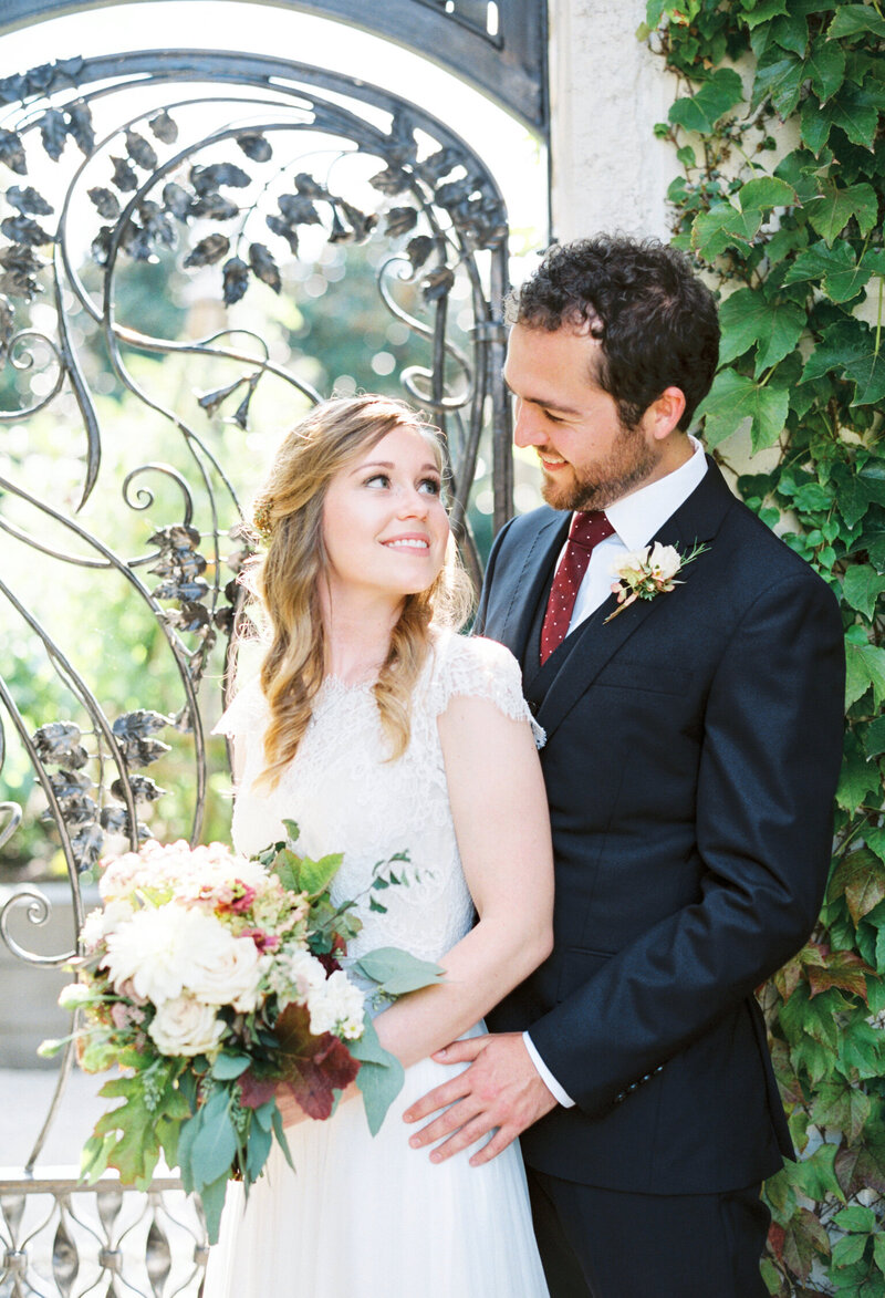 bride and groom embrace near greenery