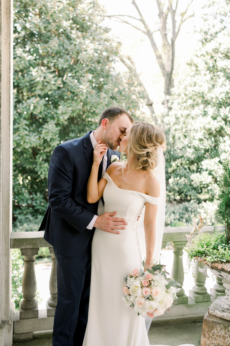 bride holding a blush rose bouquet kissing groom in a navy suit at annesdale mansion by mary kate steele
