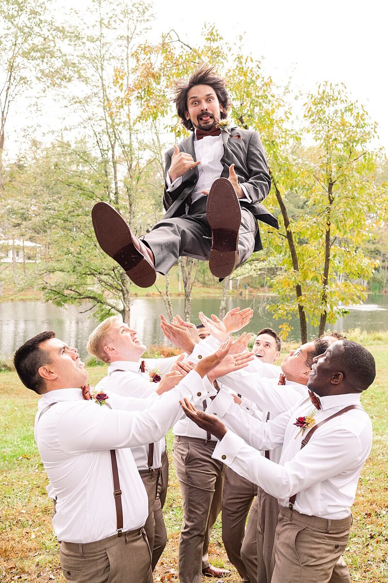 A funny bridal party photo with the groomsmen throwing the groom in the air at Avonlea Farms in Richmond, Virginia.