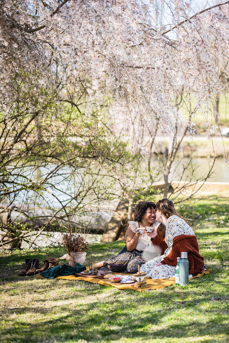 A couple goes in for a kiss as they each hold a cup of coffee while seated for their breakfast picnic at Duck Pond in Blacksburg, Virginia.