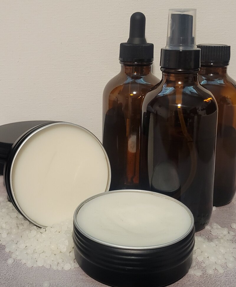 Rosemary vanilla body balm tin surrounded by amber bottles and soap crystals