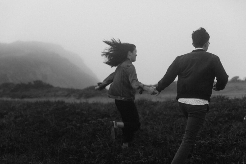black and white image couple holding hands running in field