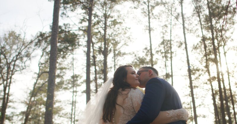 Groom kissing bride's cheek in a forest during golden hour at loblolly rise weddings