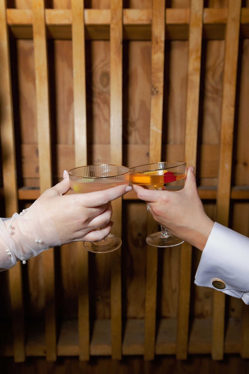 Two brides clink cocktails and cheers.