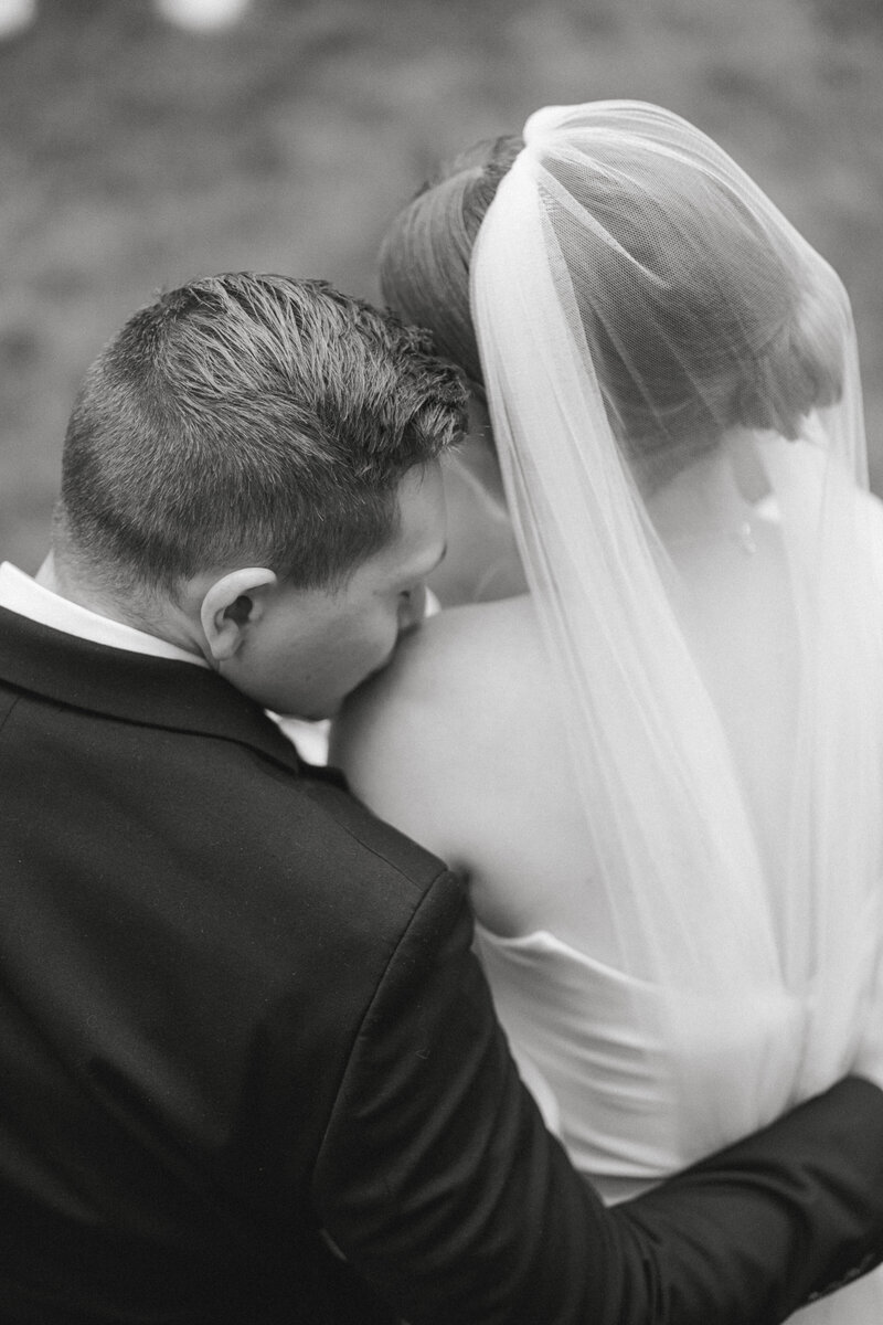 bride and groom snuggled in while groom kisses bride's shoulder