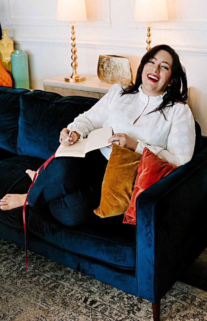 Renee Dalo smiles while journaling on navy sofa
