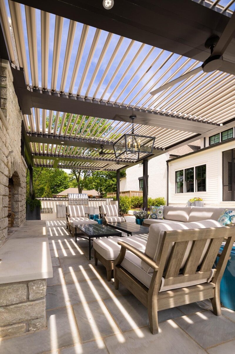 Large StruXure pergola with integrated fans and chandelier, with a stone fireplace and lots of furniture. 