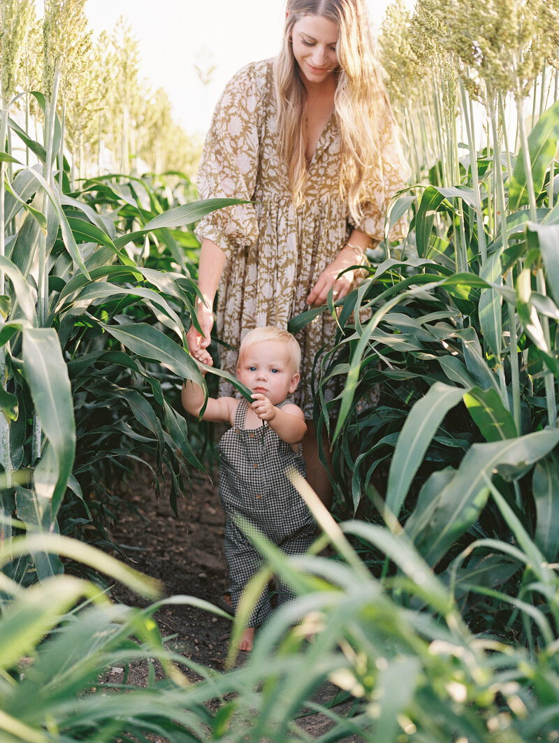 Mom in a long dress walking while holding her baby's hand through plants