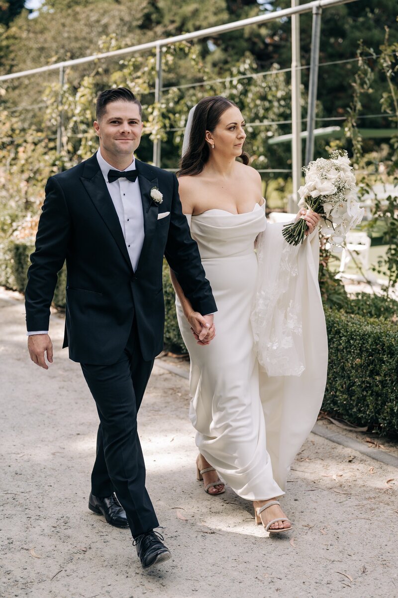 bride and groom in tuxedo walk through the queenstown gardens