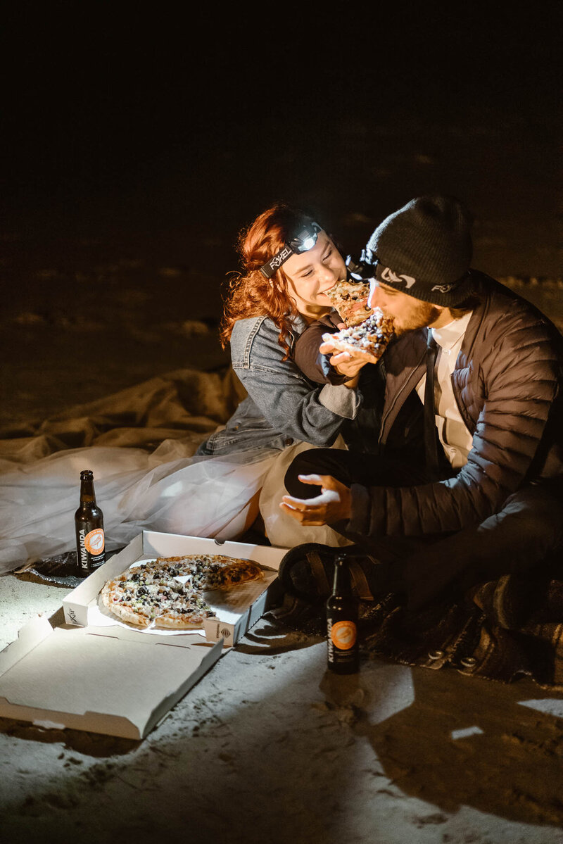 After their Oregon coast elopement a couple shares a pizza by the  light of their headlamp