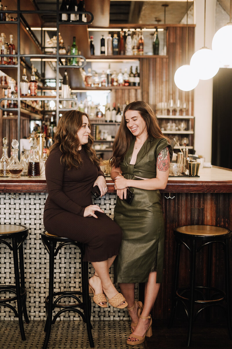Two women from Knoxville branding agency Liberty Type laugh together at a warm, modern bar