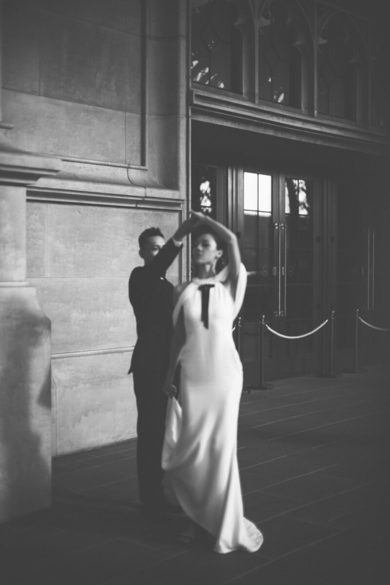 A black and white image of a groom twirling his bride around.