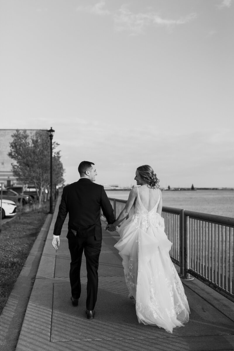 A newlywed couple holding hands and walking along a sidewalk 