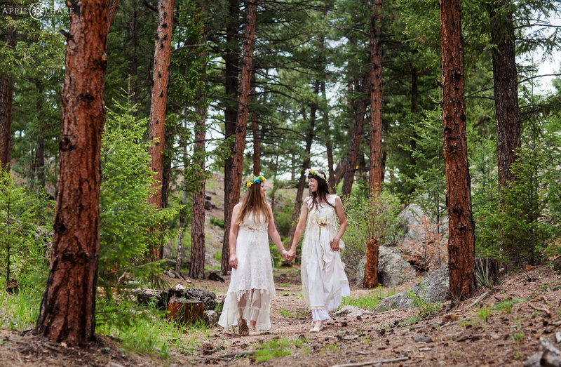 Two brides walk in the gorgeous forest trees at Bucksnort Disc Golf in Pine Colorado