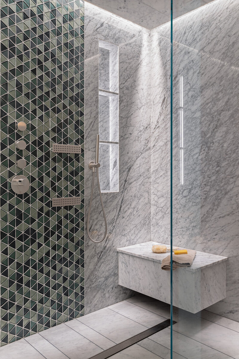 Close up shot of custom shower with floating marble bench, back-lit shelving and accent tile by Sister Studio.