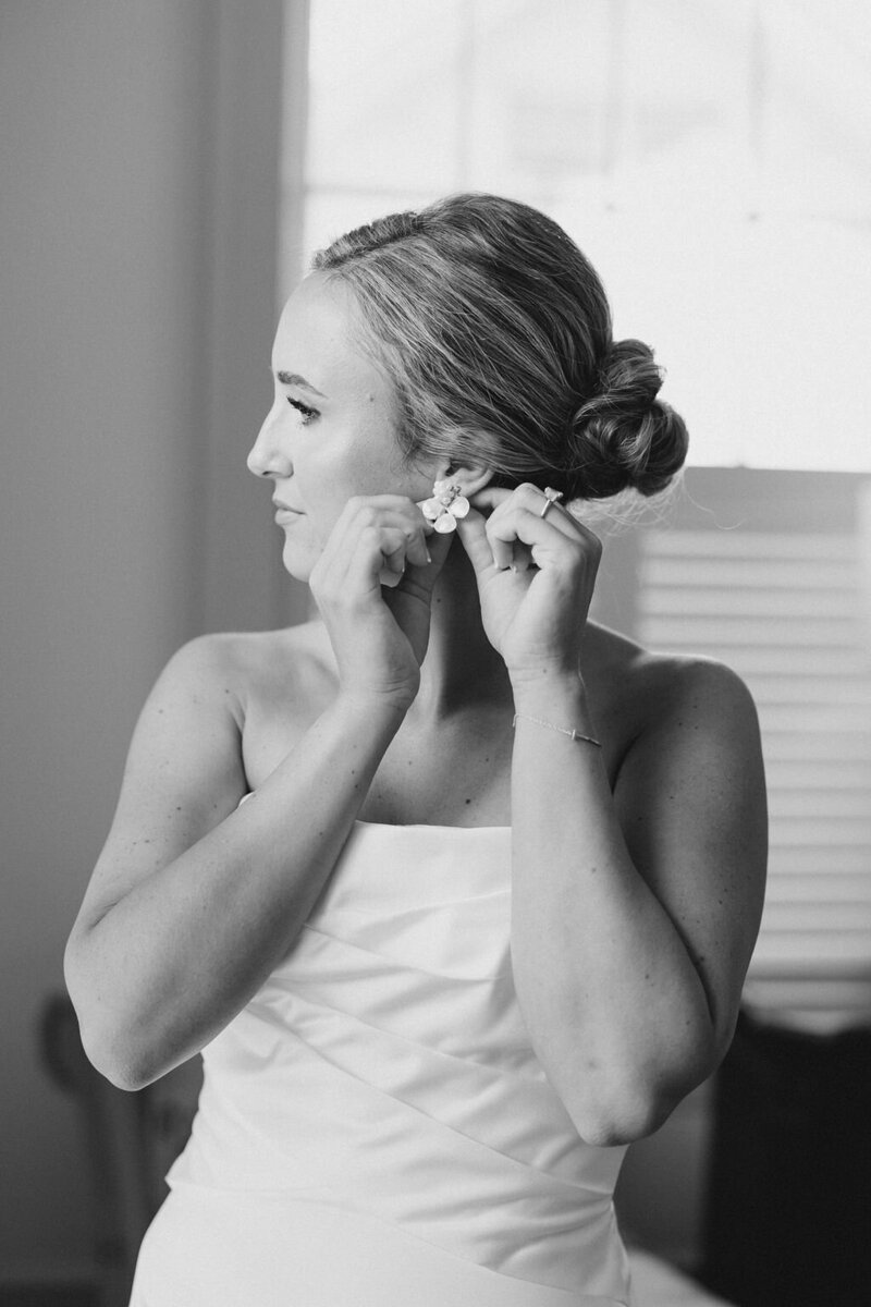 Bride in white dress with pearl earrings looks at Lake Lanier shoreline
