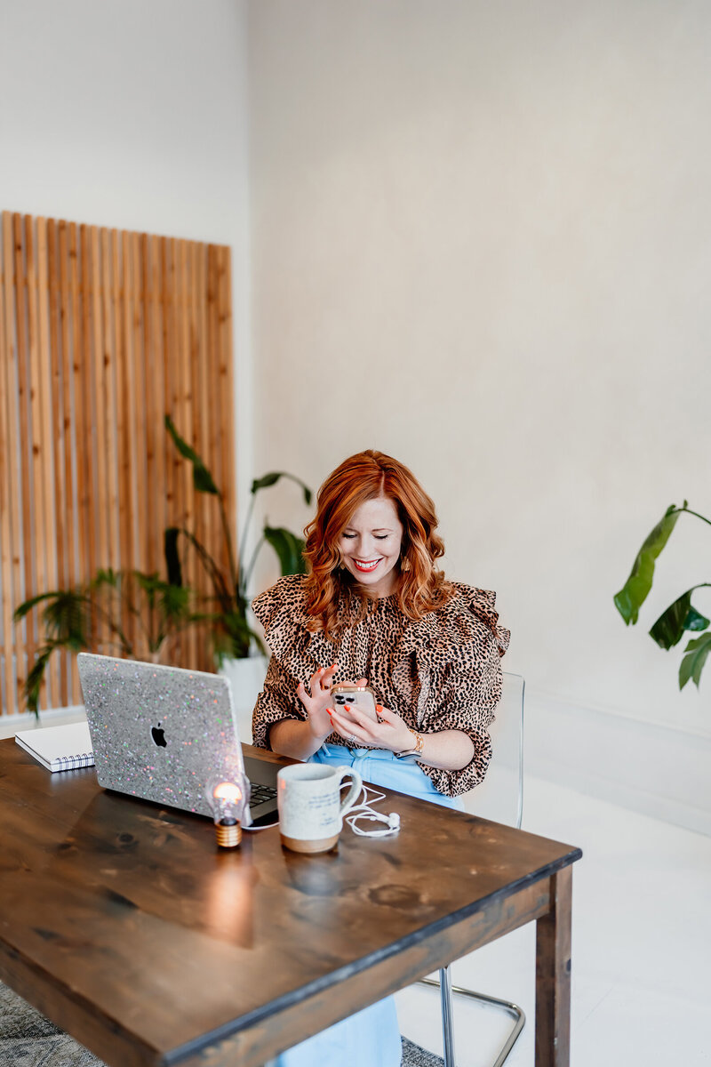 a photo of a woman who is a life coach at a desk looking at her phone and laughing