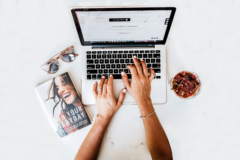 hands typing on laptop with sunglasses and book