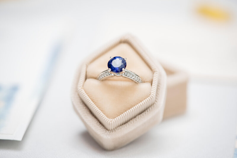 Close-up of a round saphire engagement ring nestled peach ring box.