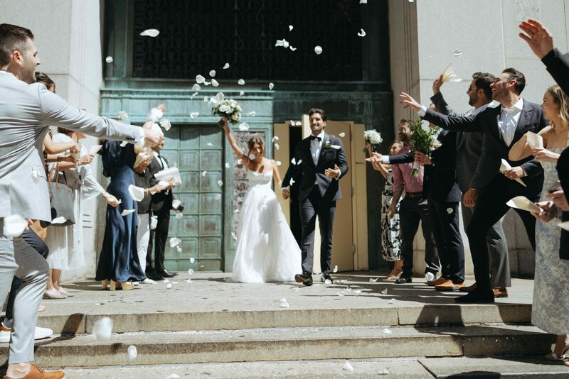 A joyful NYC micro wedding in Tribeca, with a bride and groom exiting a courthouse as guests throw flower petals in celebration.