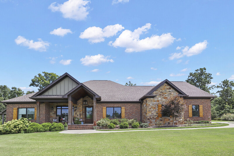 large ranch style brick home with wooden shutters and bright blue sky