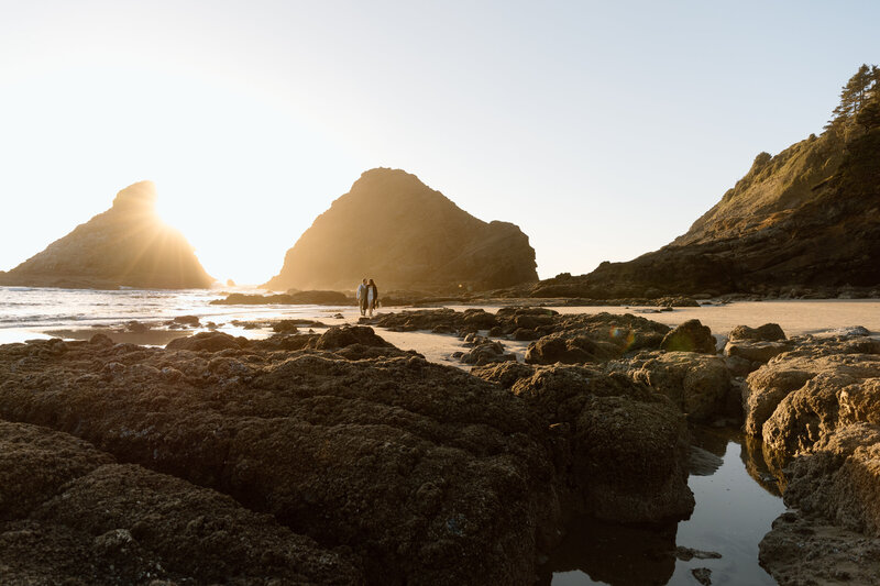 Couple walking on the beach with sea stacks behind them on the Oregon Coast.