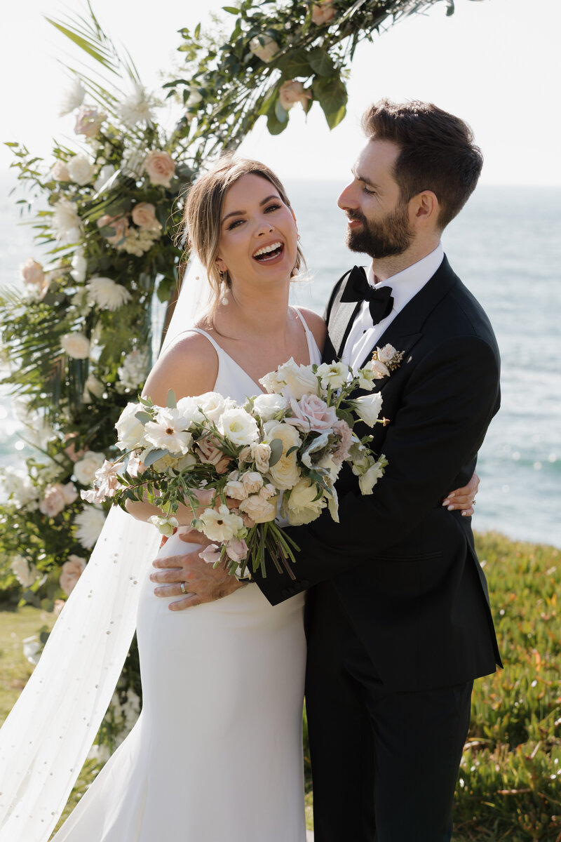 Laughing bride and groom near the ocean, captured by a luxury wedding photography team focusing on genuine, heartfelt moments.